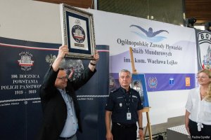 Zdjęcie przedstawia Prezesa Polskiego Związku Pływackiego z pamiątkową tabliczką otrzymaną za współpracę z Policją