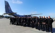 grupa policjantów na płycie lotniska w tle stoi samolot transportowy