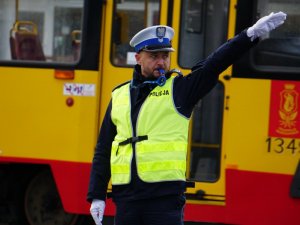 policjant z podniesioną ręką, w tle tramwaj