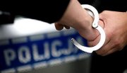 policjant zakłada na ręce podejrzanego kajdanki - z tyłu napis Policja