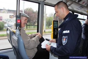 Policjant przekazuje w tramwaju ulotki profilaktyczne seniorowi