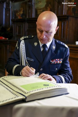 siedzący komendant głowny policji dokonuje wpisu do księgi pamiatkowej leżącej na stole