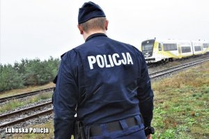 policjant przy torach kolejowych, z tyłu nadjeżdżający pociąg