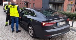 policjant po cywilnemu  w kamizelce z napisem Policja przy drzwiach kierowcy samochodu marki Audi