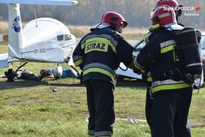 dwie osoby ranne leżące pod samolotem na płycie lotniska i trzech strażaków podczas akcji ratowniczej