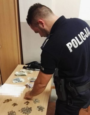 Mężczyzna ubrany w policyjny mundur przelicza pieniądze rozłożone na stole