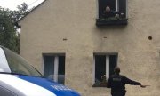 dwaj policjanci jeden stoi przed spalonym budynkiem a drugi z nich wygląda przez okno