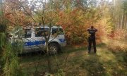 radiowóz policyjny  stojący w lesie oraz policjant w trakcie poszukiwań
