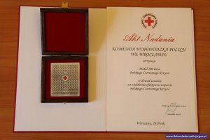 Medal 100-lecia Polskiego Czerwonego Krzyża, który otrzymała Komenda Wojewódzka Policji we Wrocławiu  oraz akt nadania