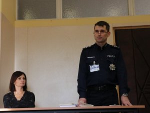 stojący policjant oraz kobieta siedząca przy stole