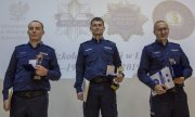 trzech najlepszych policjantów stoi na podium trzymając dyplomy i statuetki