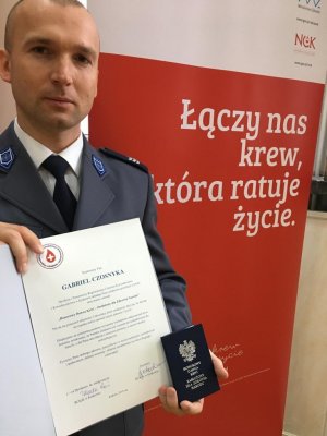policjant z medalem i listem gratulacyjnym