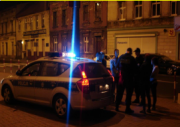 policyjny radiowóz przed budynkiem, obok stoi grupa ludzi