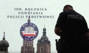 Policjant w koszulce z napisem policja, z tyłu wieże Kościoła Mariackiego. Napis: 100. rocznica powstania Policji Państwowej