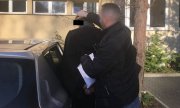 Na zdjęciu parking policyjny, policjant pilnuje zatrzymanego, pomaga mężczyźnie do wsiąść do radiowozu nieoznakowanego