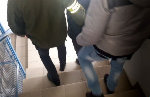 Policjanci prowadzą zatrzymanego 37-latka po schodach