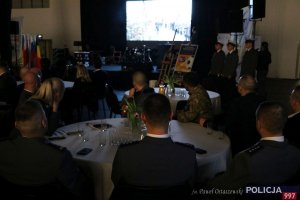 rodzina, goście oraz przedstawiciele służb mundurowych siedzą przy stole i oglądają spot filmowy podczas XI Międzynarodowego Turnieju Służb Mundurowych w Piłce Nożnej Halowej im. podkom. Andrzeja Struja