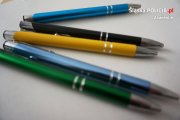 Pięć leżących długopisów w kolorach: zielony, niebieski, żółty, czarny i niebieski, z elementami koloru srebrnego