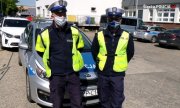 policjanci z ruchu drogowego stoją w kamizelkach odblaskowych i białych czapkach przed radiowozem