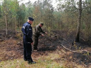 Policjant z funkcjonariuszem Straży Leśnej stojący przy wypalonym fragmencie lasu