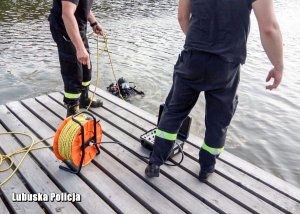 nurek podczas poszukiwań w zbiorniku wodnym, na pomoście stoją dwaj strażacy