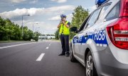 policjant przy radiowozie mierzy prędkość przejeżdżającym kierowcom