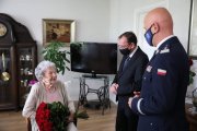 Pani Maria Czernek wraz z ministrem spraw wewnętrznych i administracji i komendantem głównym policji składającym bukiet czerwonych róż