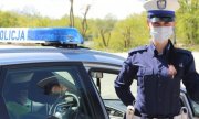 policjantka w mundurze i w maseczce stoi obok radiowozu