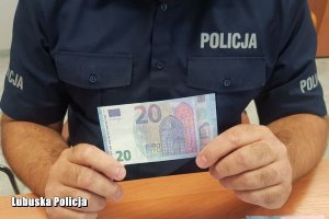policjant trzyma fałszywy banknot