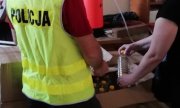 policjant w kamizelce z napisem POLICJA podczas przekazywania pracownikowi sanepidu 334 butelek spirytusu zapakowanego w kartonowych pudłach