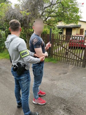 Na fotografii widać policjanta, który trzyma za rękę zatrzymanego mężczyznę. Sprawca wskazuje na dom, do którego się włamał.&quot;&gt;