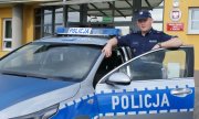 Umundurowany policjant stoi przy oznakowanym radiowozie, przed siedzibą Komendy Powiatowej Policji w Wieruszowie