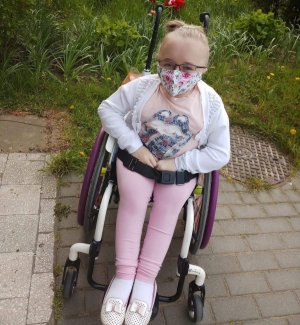 dziewczynka w maseczce na twarzy na wózku inwalidzkim