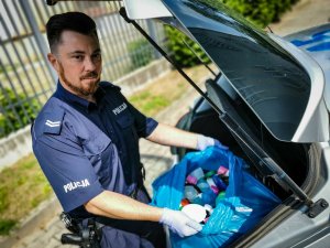 policjant wyciąga worek z nakrętkami z bagażnika samochodu