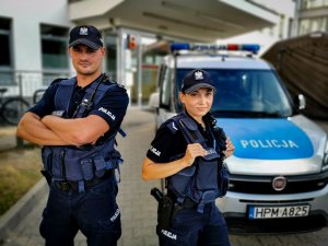 policjant i policjantka stoją przed radiowozem
