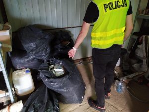 Policjant dokonujący zabezpieczenia materiałów znalezionych w nielegalnym laboratorium służącym do produkcji substancji psychotropowych.