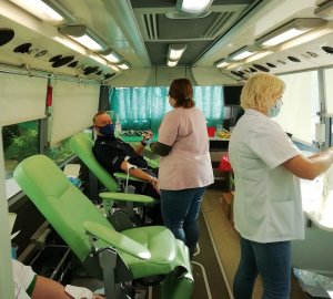 krwiodawcy siedzą na fotelach w ambulansie, którego obsługa prowadzi pobór krwi&quot;&gt;