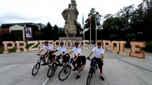 Czterech policjantów na rowerach ustawionych obok siebie, w tle neonowy napis &quot;Przebojowe Opole&quot;.