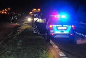 noc - policyjny radiowóz na sygnałach stoi przy drodze na miejscu wypadku, w oddali widać policjantów