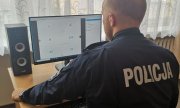policjant w mundurze  z napisem &quot;Policja&quot; na plecach, siedzi przed komputerem