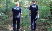 dwóch umundurowanych policjantów prowadzących poszukiwania w lesie