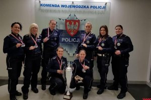 Drużyna Wielkopolskiej Policji Kobiet w Piłce Nożnej w mundurach policyjnych z medalami na szyi, w tle logo policji wielkopolskiej