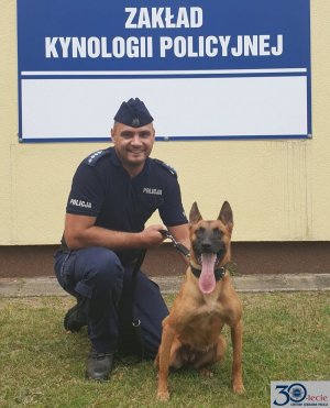 policjant z psem, w tle na budynku napis Zakład Kynologii Policyjnej