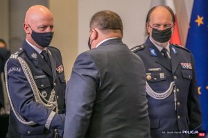 Komendant Główny Policji gratuluje odznaczonemu, w tle Przewodniczący NSZZ Policjantów.
