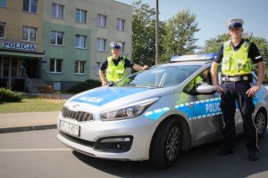dwaj umundurowani policjanci ruchu drogowego stoją przy radiowozie