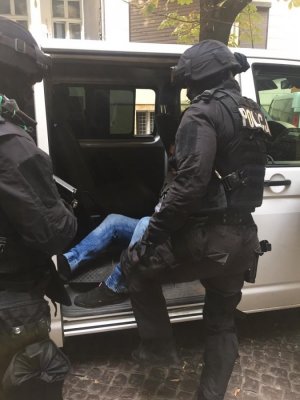 dwaj policjanci z grupy realizacyjnej przed samochodem, w środku auta widać nogi zatrzymanego mężczyzny