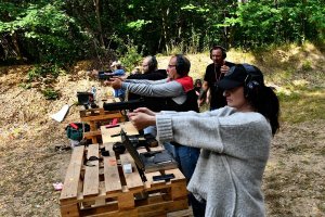 kobieta i mężczyźni biorący udział w zawodach strzeleckich celują z broni