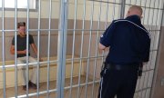 zatrzymany mężczyzna siedzi za kratami w areszcie, policjant zamyka zamek
