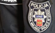 Na mundurze napis POLICJA oraz naszywka z napisem Komenda Miejska Policji w Łodzi a pośrodku naszywki znajduje się odznaka policyjna z herbem Łodzi