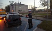 umundurowany policjant w białej czapce  stoi obok zaparkowanego na miejscu dla niepełnosprawnych vw , który za chwile będzie wciągany na widoczną przed nim lawetę